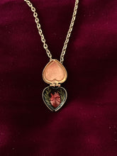 Load image into Gallery viewer, Inside the heart-shaped pendant is a miniature anatomical painting of a human heart on a black background. There is a green leafed-branch on each side of the heart.